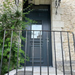 La porte d'entrée vitrée Spencer et sa grille volute sur une charmante façade de maison en pierre